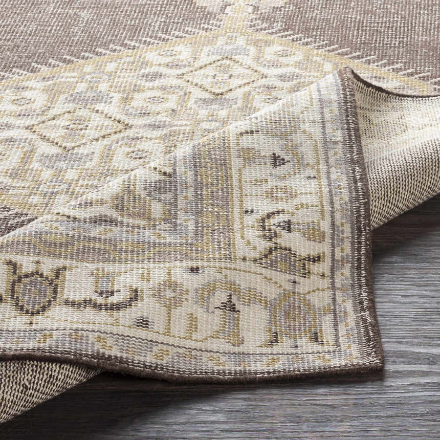Close-up of the hand-knotted Clyo Carpet. Brown, charcoal, and off-white farmhouse style rug with a folded corner. Fold