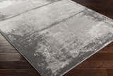 Close-up of the Coombs Area Rug on dark wood flooring. The rug has a contemporary gray abstract design. Corner