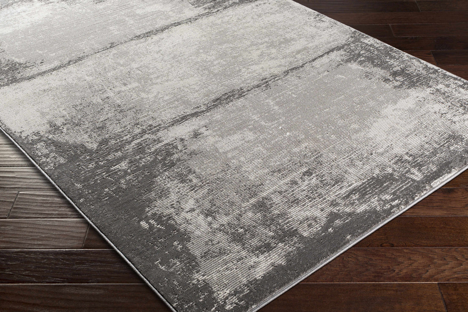 Close-up of the Coombs Area Rug on dark wood flooring. The rug has a contemporary gray abstract design. Corner