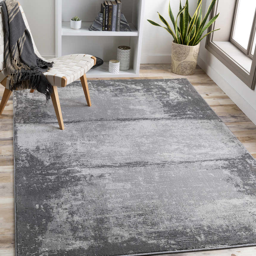 Modern living room scene with a gray and charcoal Coombs Area Rug, woven chair, and white bookshelf. Roomscene-Rectangle
