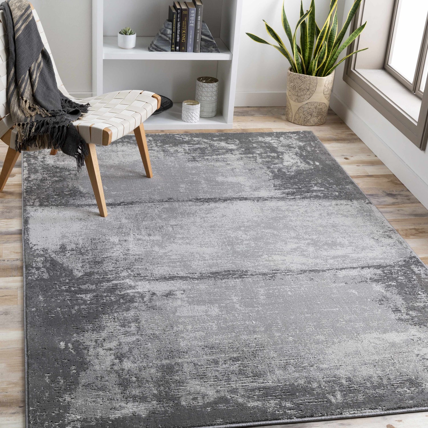 Modern living room scene with a gray and charcoal Coombs Area Rug, woven chair, and white bookshelf. Roomscene-Rectangle