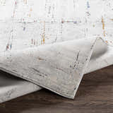 Close-up of the Concordia Faux Silk Rug showing its off-white base with burgundy, burnt orange, and blue abstract pattern. Fold