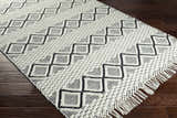 Close-up of the Cobourg Area Carpet. Hand woven, cream and black geometric design with fringe detail. 100% wool rug. Corner