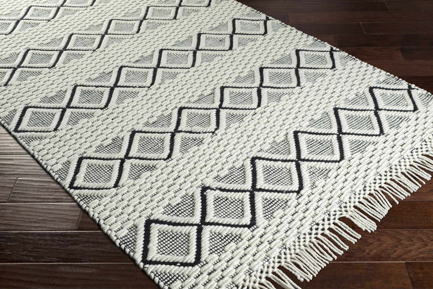 Close-up of the Cobourg Area Carpet. Hand woven, cream and black geometric design with fringe detail. 100% wool rug. Corner