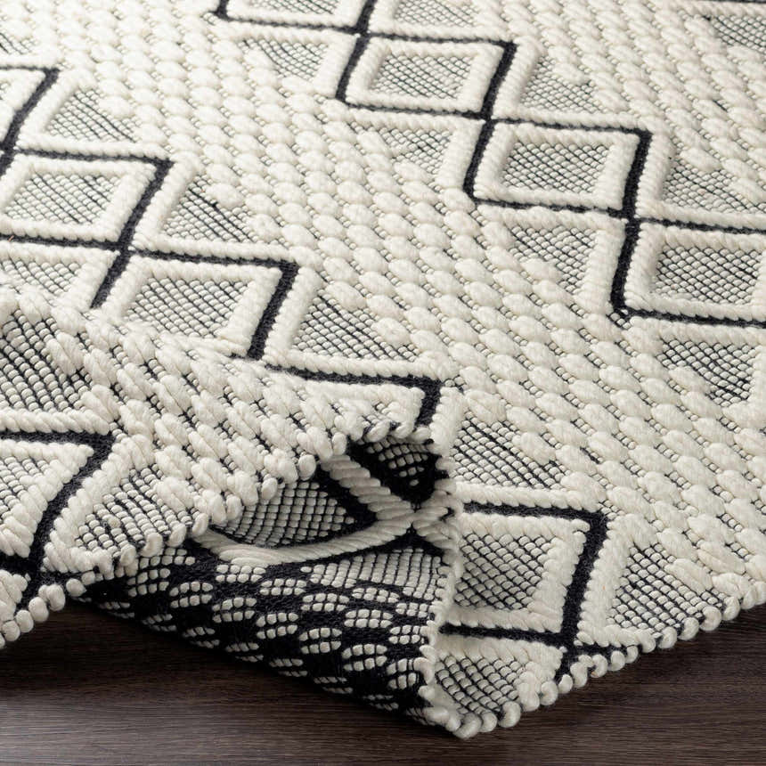Close-up of the hand-woven Cobourg Area Carpet. Black geometric diamonds on a cream wool rug with a textured, looped pile. Fold