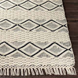 Close-up of the hand woven Cobourg Area Carpet. Cream wool rug with black geometric diamond pattern and fringed edge. Front