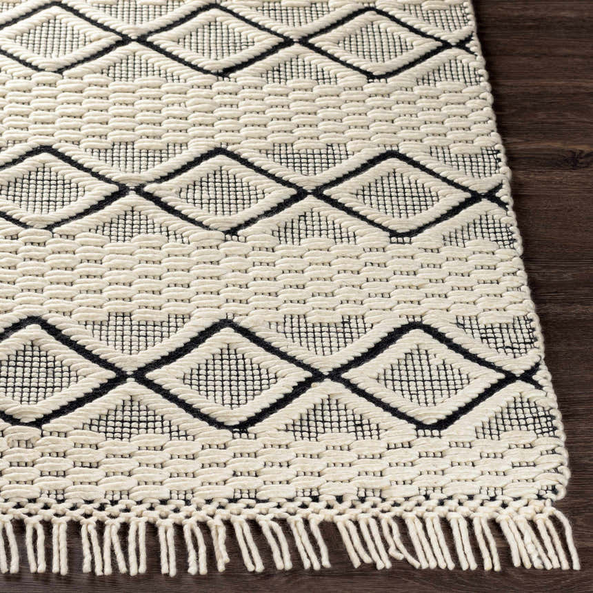 Close-up of the hand woven Cobourg Area Carpet. Cream wool rug with black geometric diamond pattern and fringed edge. Front