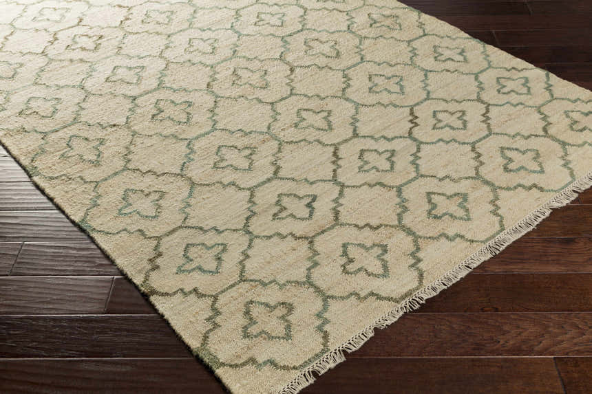 Coffeyville jute rug, cream and sage geometric pattern, fringed edge, on dark wood floor. Handcrafted, contemporary style. Corner