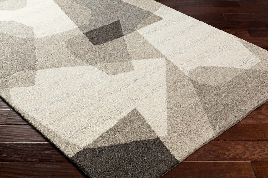 Close-up of the hand-tufted Colin Area Rug. Geometric design in beige, bone, dark brown, and gray wool on a hardwood floor. Corner