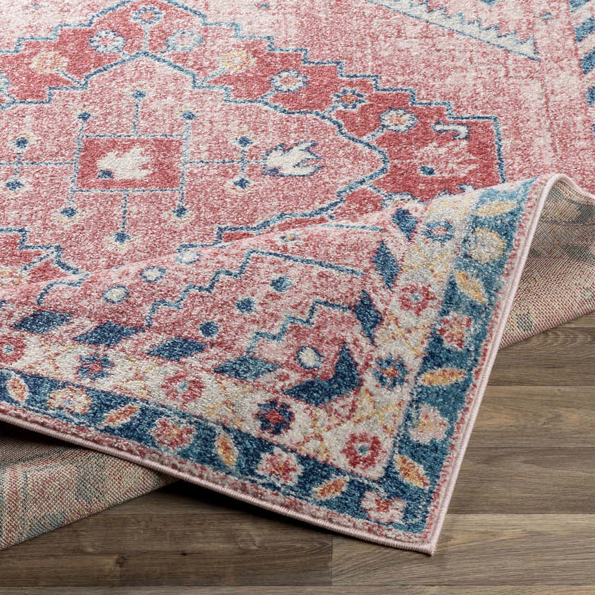 Close-up of the Conder Area Rug showing its bohemian, oriental design in pink, red, and blue on a wood floor. Fold