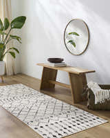 Entryway with a Scandi Moroccan Trellis Rug, wood bench, round mirror, and potted plant for a bright, minimalist look. Roomscene-Runner