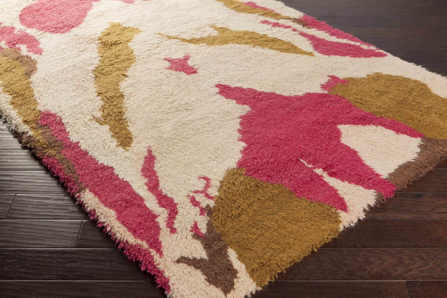 Close-up of the Crenshaw Carpet. Hand-woven wool shag rug in dark brown, light pink, and mustard on dark wood floors. Corner