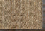 Close-up of the Buwoi Hand Woven Tan Jute Rug showing its diamond pattern, natural jute texture, and dark wood floor. Corner