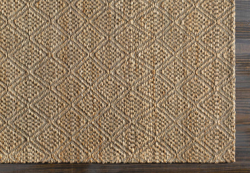 Close-up of the Buwoi Hand Woven Tan Jute Rug showing its diamond pattern, natural jute texture, and dark wood floor. Corner