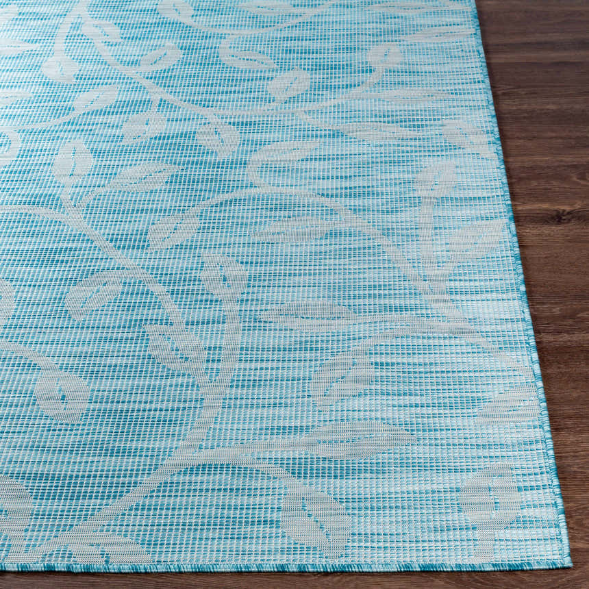 Close-up of Cairnlea Area Rug in aqua with a white floral vine pattern on a dark wood floor. Coastal style. Front