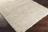 Close-up of a hand-woven Carrier Clearance Jute Carpet. Natural fiber rug with charcoal and ivory woven pattern on dark wood floor. Corner