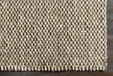 Close-up of the hand-woven Carrier Clearance Jute Carpet. Natural fiber rug with charcoal and ivory tones. Corner