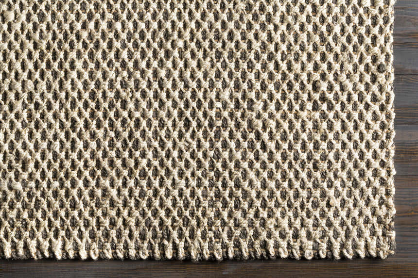 Close-up of the hand-woven Carrier Clearance Jute Carpet. Natural fiber rug with charcoal and ivory tones. Corner
