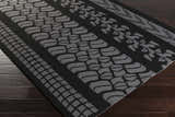 Close-up of the hand-hooked Cressona Area Rug. Black rug with geometric gray patterns on dark wood floor. Corner