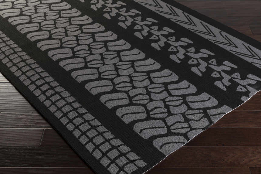 Close-up of the hand-hooked Cressona Area Rug. Black rug with geometric gray patterns on dark wood floor. Corner