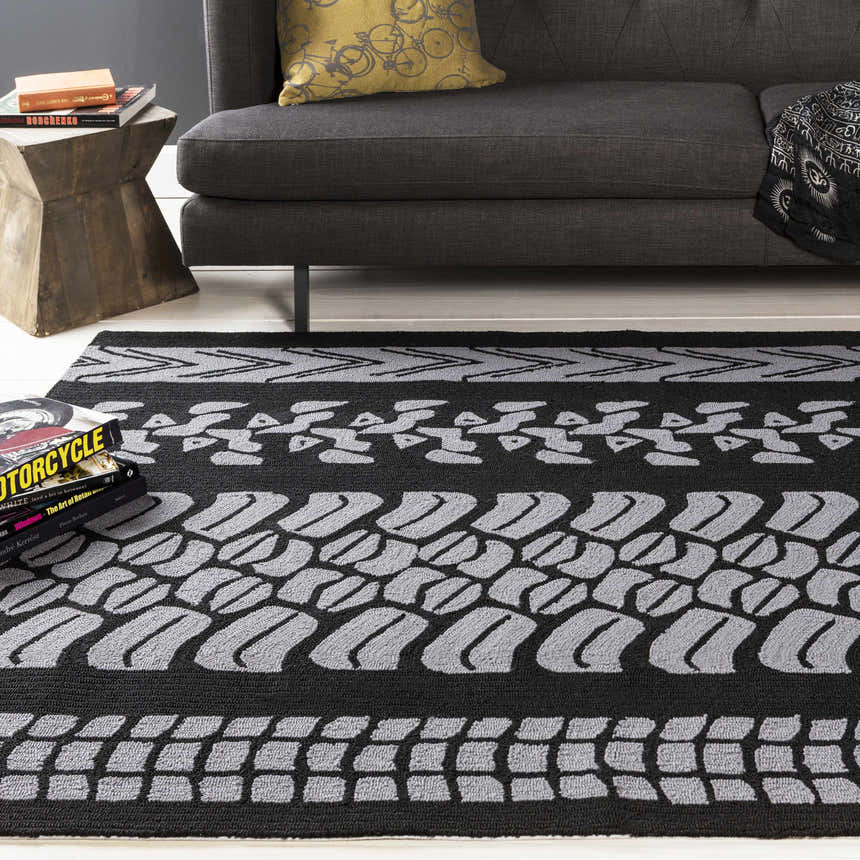 Living room scene with a gray couch and a black and gray Cressona Area Rug with a tire track design. Styleshot