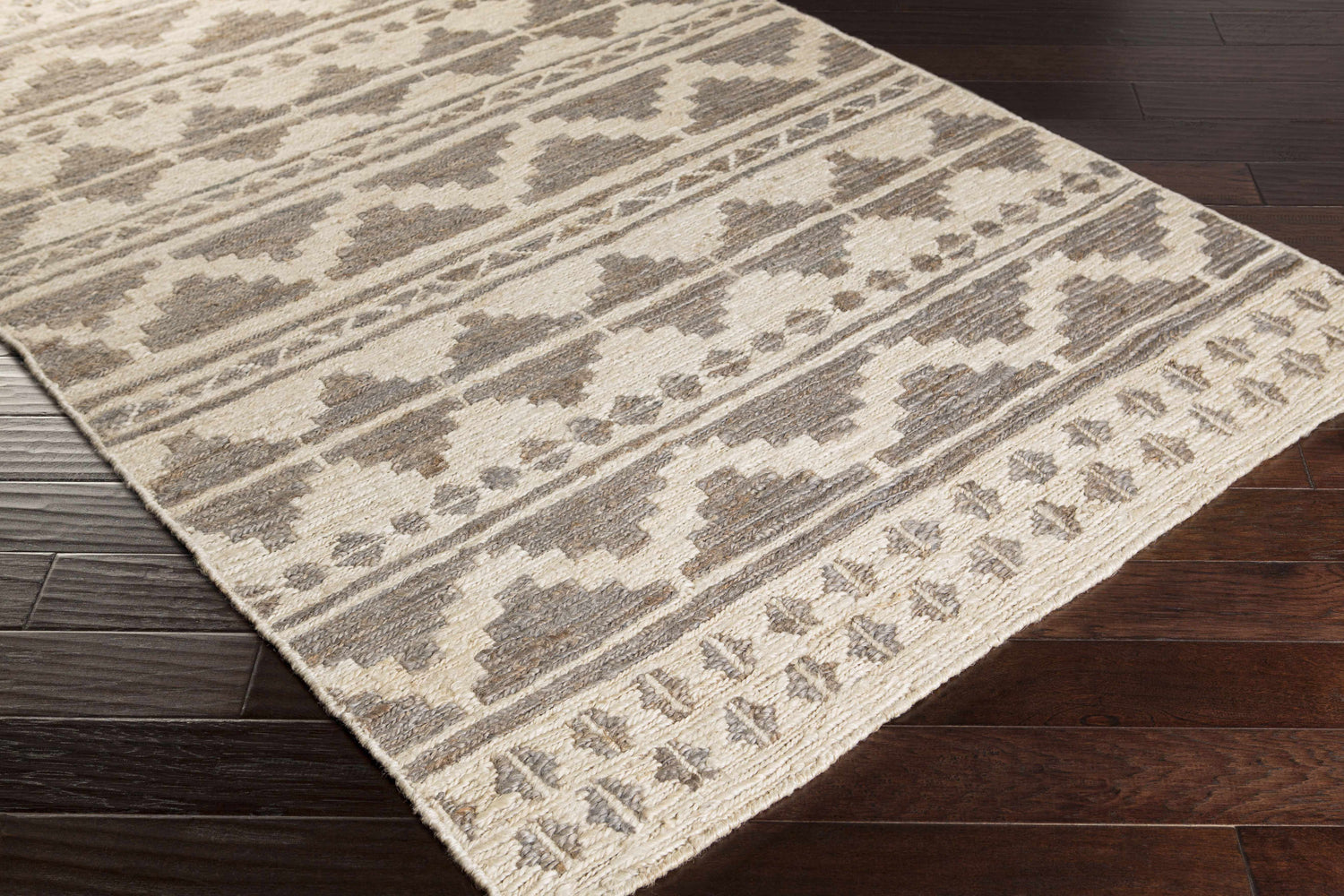 Close-up of the hand woven Cresco Jute Carpet. Farmhouse style rug in charcoal, dark brown, and ivory on dark wood floors. Corner