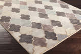 Close-up of the hand-knotted Cuero Area Rug. Charcoal, light brown, and taupe quatrefoil pattern on dark wood floor. Corner