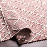 Close-up of the Dacudao Area Rug. Hand woven wool rug in burgundy, cream, and dusty pink with a geometric diamond pattern. Fold