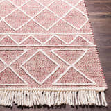 Close-up of the Dacudao Area Rug. Hand-woven wool rug in burgundy, cream, and dusty pink with geometric patterns and fringe. Front