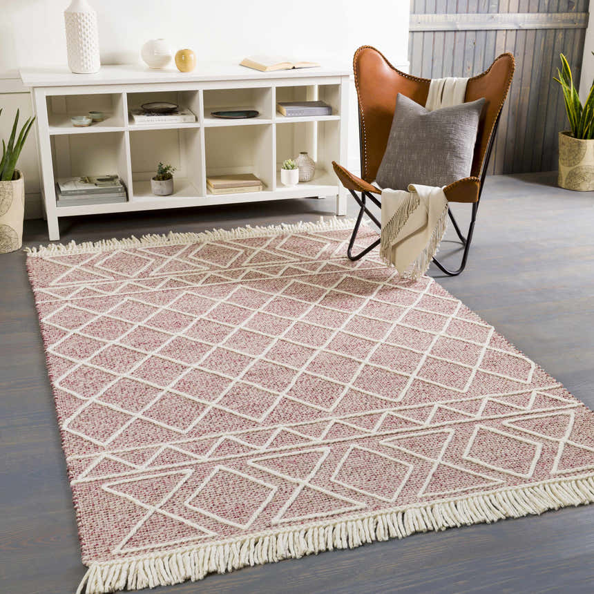 Living room scene with a burgundy and cream Dacudao Area Rug. Geometric pattern, fringe, leather chair, and white shelving unit. Roomscene-Rectangle