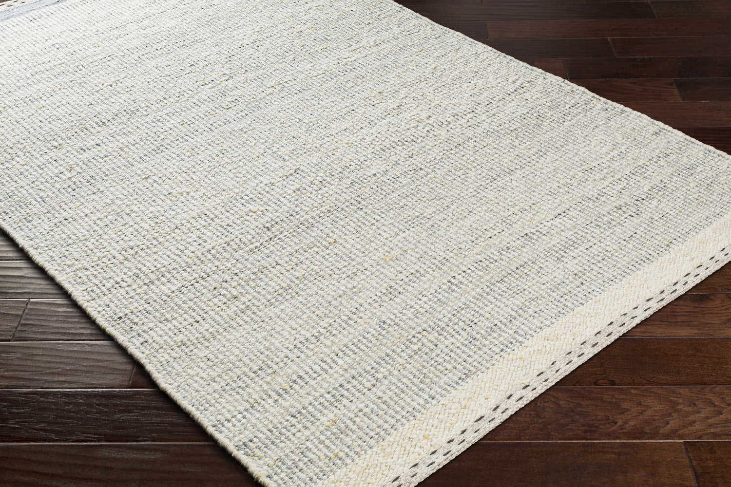 Close-up of Dalaoig Flat Woven Wool Rug. Charcoal, cream, and gray tones. Hand woven texture on dark wood floor. Corner