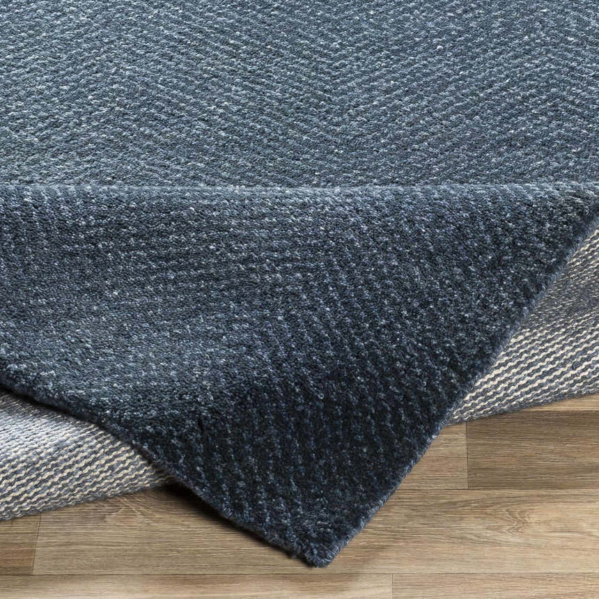 Close-up of the hand-knotted Dateland Area Rug showing its navy and pale blue wool and viscose texture and herringbone pattern. Fold