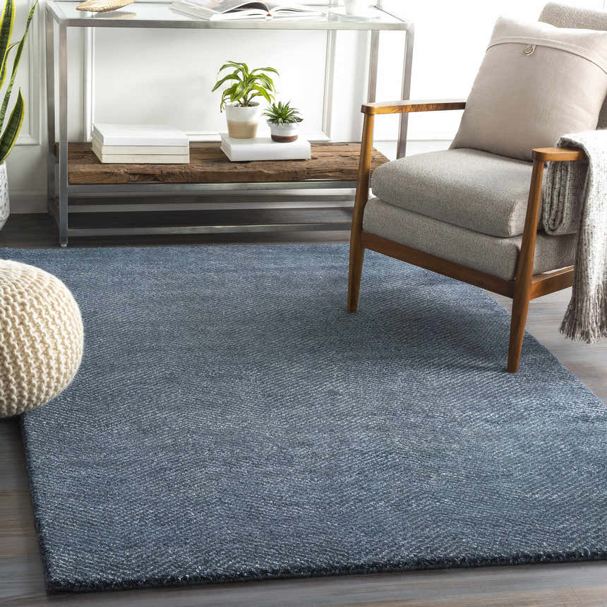 Living room scene with a navy Dateland Area Rug, gray chair, and knit pouf. Roomscene-Rectangle