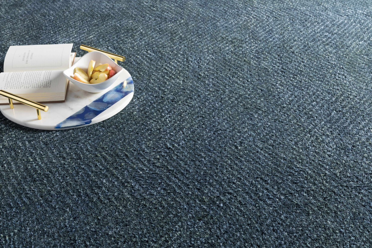 Close-up of the navy and pale blue Dateland Area Rug, with a book and fruit bowl on a marble tray. Styleshot
