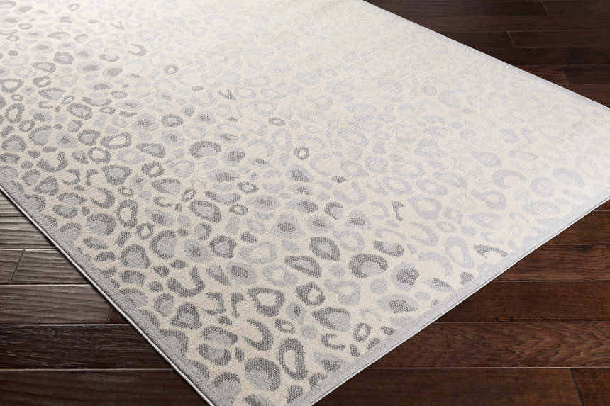 Close-up of the Delphia Cheetah Print Area Rug in gray, light slate, and oatmeal on dark wood flooring. Corner