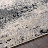 Close-up of the Dumangas Area Rug, showcasing its contemporary black, charcoal, cream, and gray abstract pattern and soft texture. Texture