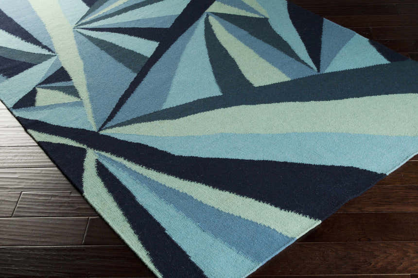 Close-up of the Dennis Area Rug. Hand-woven wool rug with a contemporary geometric design in aqua, blue, navy, and sage. Corner