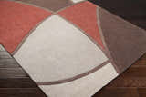 Close-up of the Docena Carpet, a hand-tufted rug with beige, rust, and brown geometric shapes on a dark wood floor. Corner