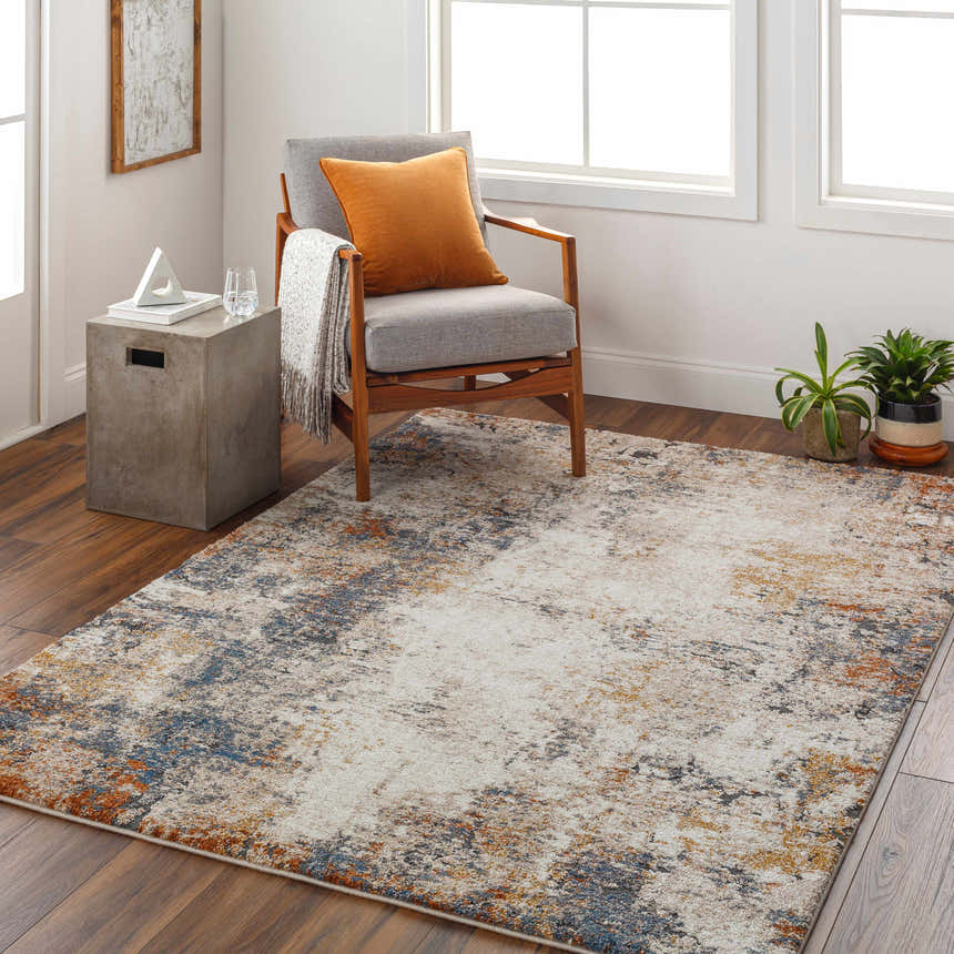 Living room scene with a Donar Thick Luxe Rug in beige, blue, and orange tones, styled with a gray chair and wood floors. Roomscene-Rectangle