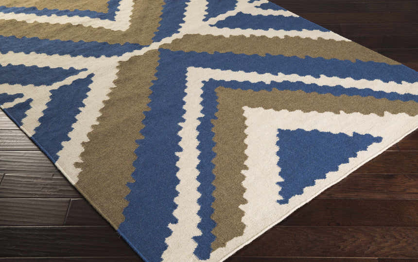 Close-up of the Doncaster Area Rug. Hand woven wool rug with charcoal, dark blue, and light beige geometric pattern. Corner