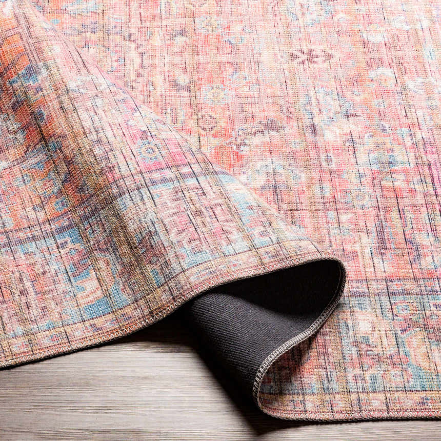 Close-up of Dormont Washable Area Rug showing its coral, cream, and blue oriental pattern and texture on a wood floor. Fold