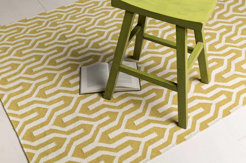 Close-up of Drewryville Area Carpet featuring a tan and white geometric pattern with a green stool and book. Styleshot