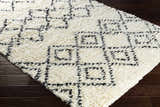 Close-up of the hand woven Dukedom Area Rug. Ivory shag rug with a black geometric pattern on dark wood floors. Corner