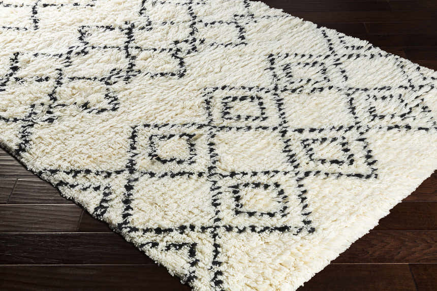 Close-up of the hand woven Dukedom Area Rug. Ivory shag rug with a black geometric pattern on dark wood floors. Corner