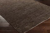 Close-up of the black Dummerston Jute Carpet showing texture and a white border on dark wood floors. Corner