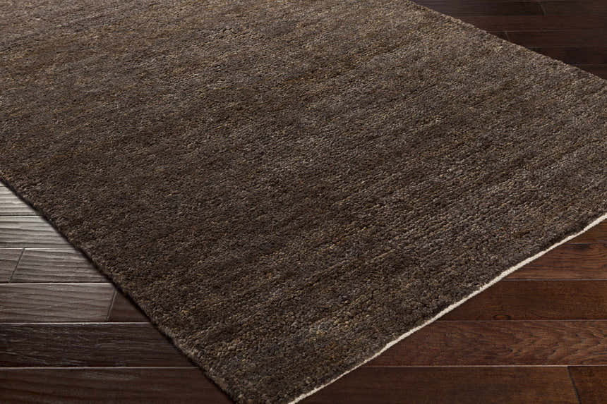 Close-up of the black Dummerston Jute Carpet showing texture and a white border on dark wood floors. Corner