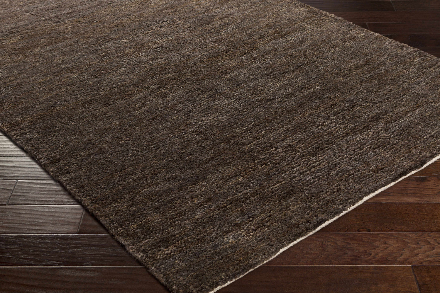 Close-up of the black Dummerston Jute Carpet showing texture and a white border on dark wood floors. Corner