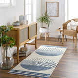 Hallway scene with a blue geometric Duri Area Rug, wood console table, plants, and wicker chair. Roomscene-Runner