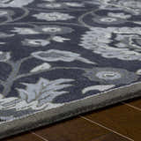 Close up of the Conesus Hand Tufted Blue Area Rug showing its floral pattern, wool texture, and charcoal, denim, and slate blue colors. Texture