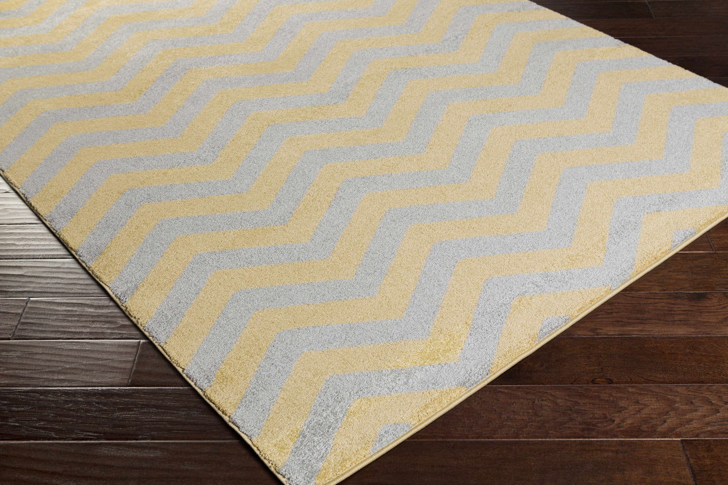 Close-up of the Eloy Area Rug. Charcoal and mustard chevron pattern on a soft, machine-woven polypropylene rug. Corner